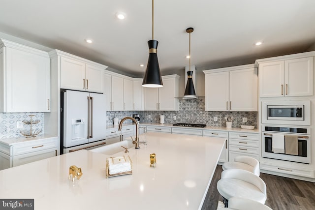 kitchen with wall chimney exhaust hood, sink, white cabinetry, decorative light fixtures, and appliances with stainless steel finishes