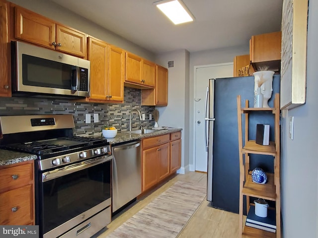 kitchen with visible vents, a sink, tasteful backsplash, stainless steel appliances, and dark stone counters