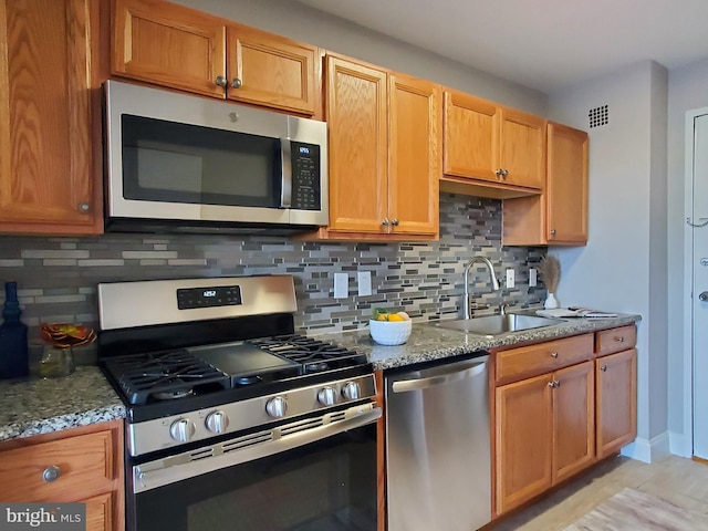 kitchen with a sink, light stone counters, visible vents, and stainless steel appliances