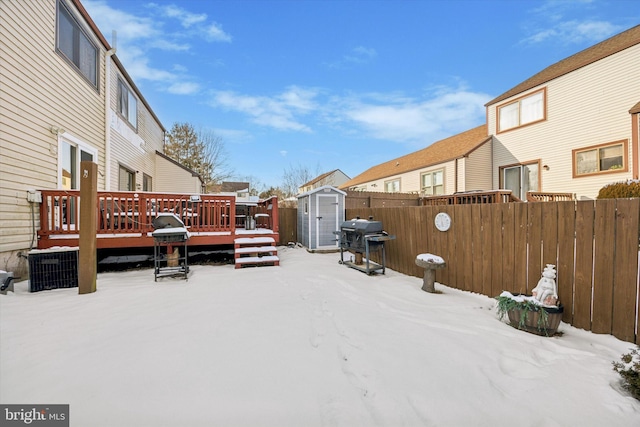 snowy yard featuring a wooden deck and a storage unit