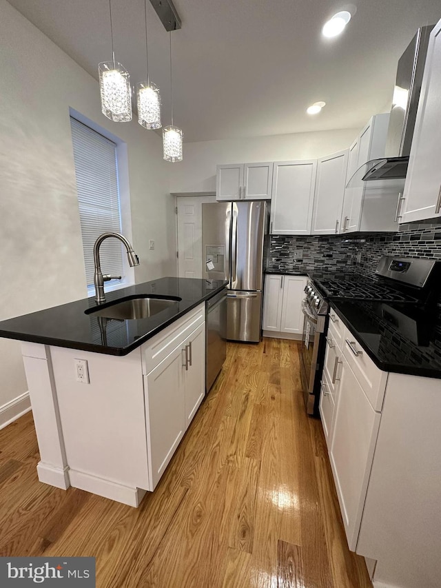 kitchen with sink, stainless steel appliances, an island with sink, white cabinets, and wall chimney exhaust hood