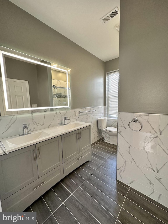 bathroom with vanity, toilet, and tile walls