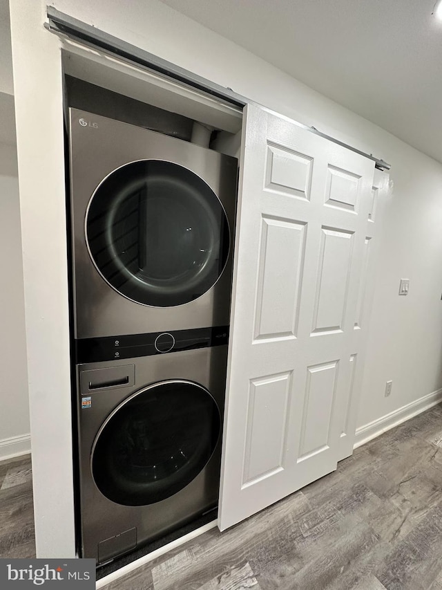 clothes washing area featuring wood-type flooring and stacked washer / dryer