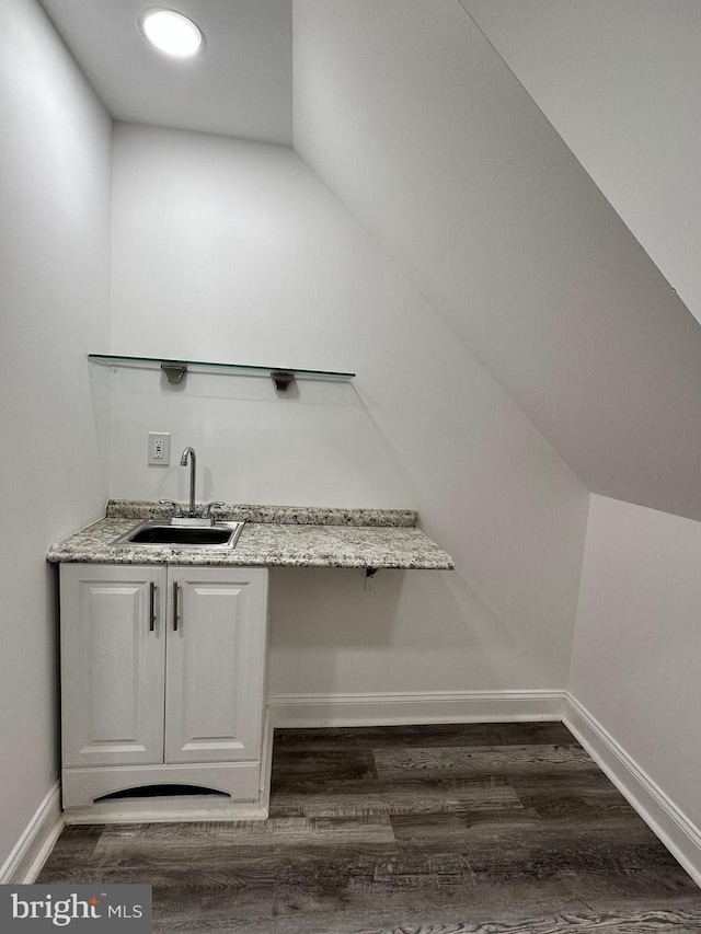 bar with dark wood-type flooring, sink, light stone counters, vaulted ceiling, and white cabinets