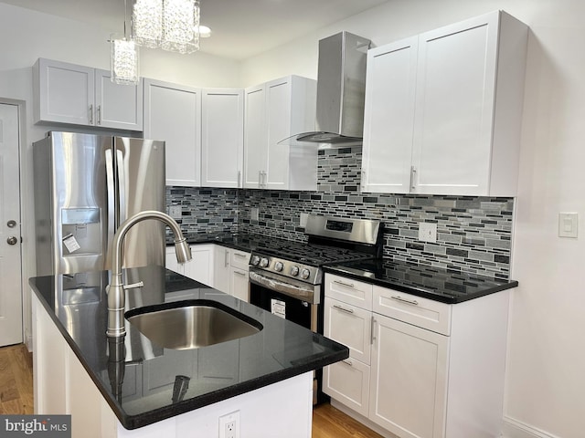 kitchen with appliances with stainless steel finishes, pendant lighting, decorative backsplash, a kitchen island with sink, and wall chimney range hood