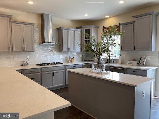 kitchen with appliances with stainless steel finishes, wall chimney exhaust hood, gray cabinets, and a kitchen island