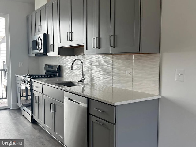 kitchen with sink, decorative backsplash, gray cabinets, and stainless steel appliances