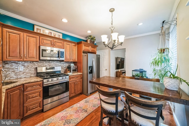 kitchen with an inviting chandelier, appliances with stainless steel finishes, pendant lighting, light stone countertops, and backsplash