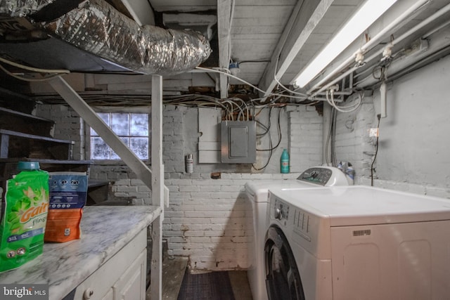 clothes washing area featuring brick wall, washer and clothes dryer, and electric panel