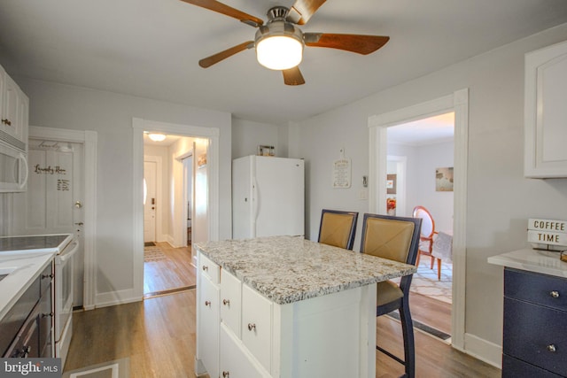 kitchen featuring a kitchen island, white cabinetry, a kitchen bar, white appliances, and light wood-type flooring