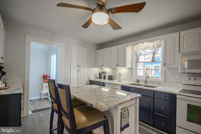 kitchen with sink, white appliances, a kitchen breakfast bar, a center island, and white cabinets