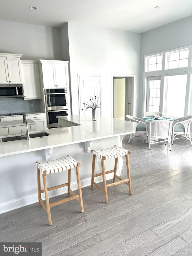 kitchen with a breakfast bar, sink, white cabinets, stainless steel appliances, and light wood-type flooring