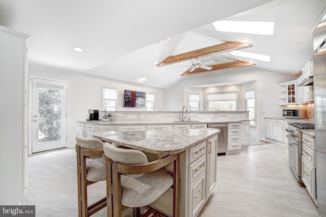 kitchen with a kitchen island, lofted ceiling with skylight, stainless steel appliances, light stone counters, and a kitchen bar