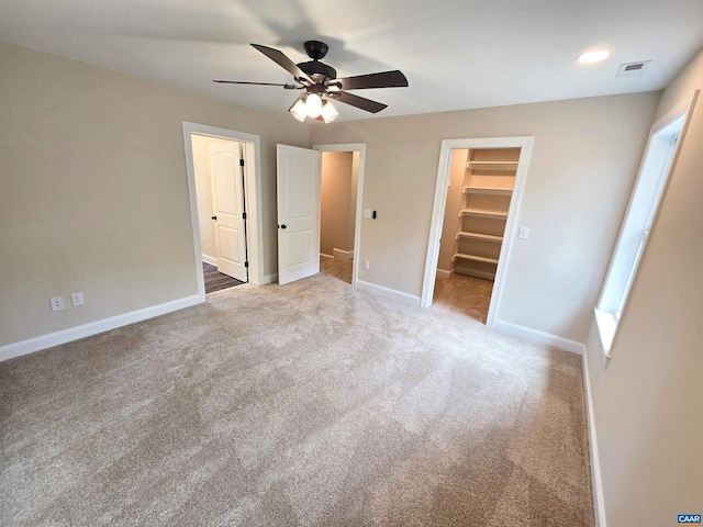 unfurnished bedroom featuring a walk in closet, carpet floors, ceiling fan, and a closet