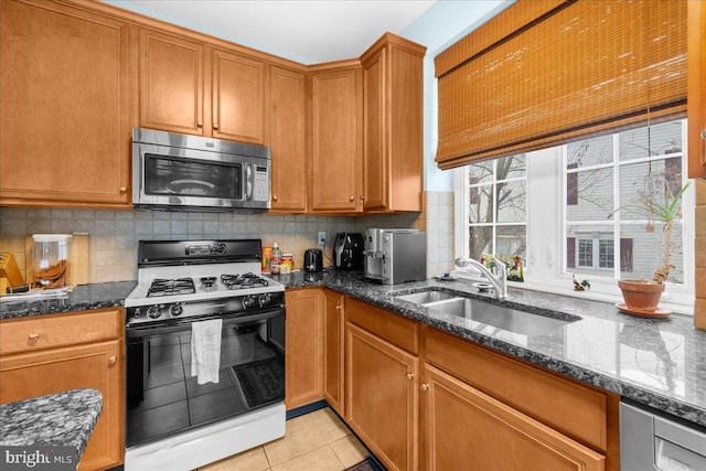 kitchen with gas range, dark stone counters, light tile patterned flooring, and sink