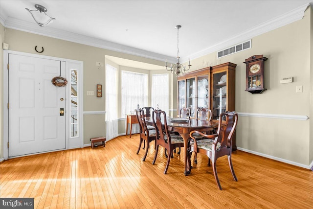 dining area with an inviting chandelier, ornamental molding, and light hardwood / wood-style flooring