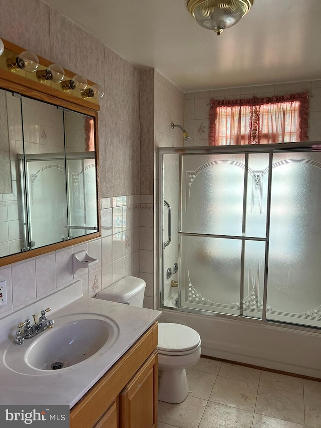 full bathroom featuring combined bath / shower with glass door, tile walls, vanity, tile patterned floors, and toilet