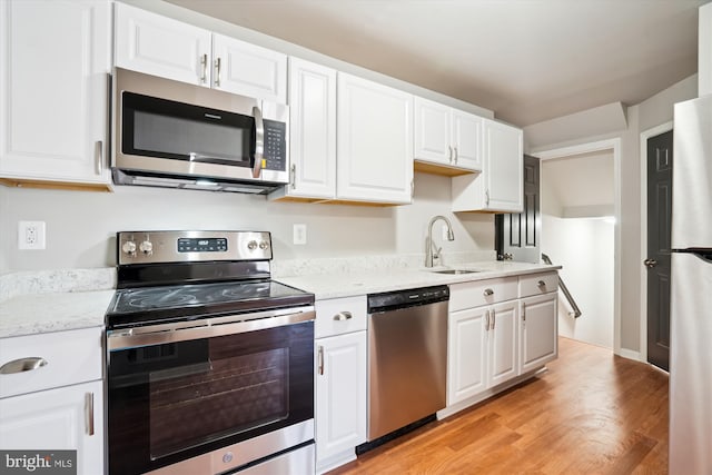 kitchen with sink, white cabinetry, light stone counters, stainless steel appliances, and light hardwood / wood-style floors