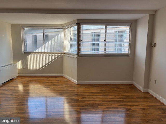 unfurnished room featuring dark hardwood / wood-style floors, radiator, and a wealth of natural light