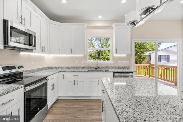 kitchen featuring sink, white cabinetry, hardwood / wood-style floors, stainless steel appliances, and light stone counters