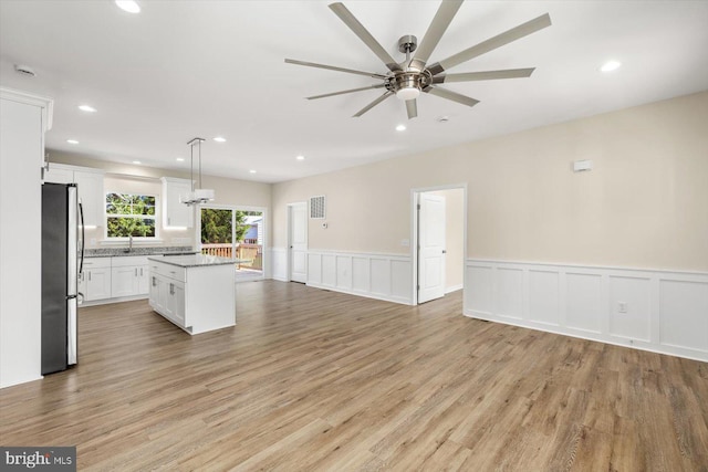 kitchen with a center island, hanging light fixtures, stainless steel fridge, light hardwood / wood-style floors, and white cabinets