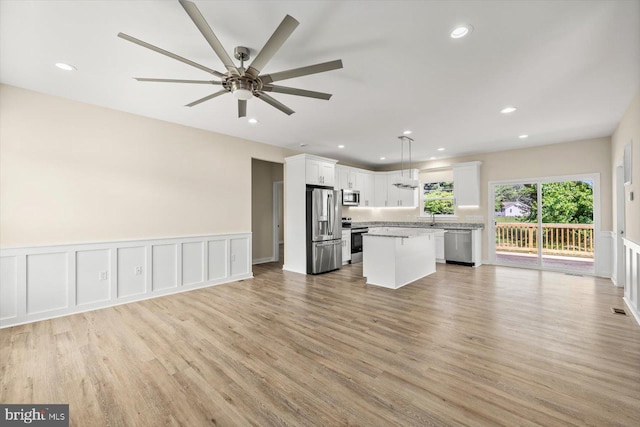 kitchen featuring a kitchen island, decorative light fixtures, white cabinets, light stone counters, and stainless steel appliances