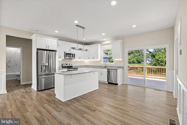 kitchen featuring white cabinetry, hanging light fixtures, appliances with stainless steel finishes, a kitchen island, and light stone countertops