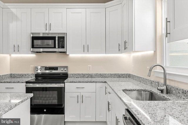 kitchen with stainless steel appliances, white cabinetry, light stone countertops, and sink