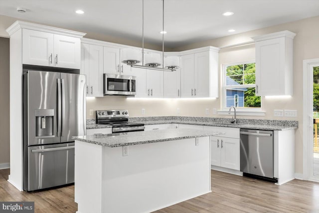 kitchen with a kitchen island, appliances with stainless steel finishes, white cabinetry, sink, and light stone counters