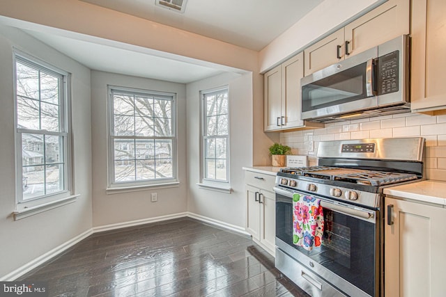 kitchen with appliances with stainless steel finishes, light countertops, backsplash, and baseboards