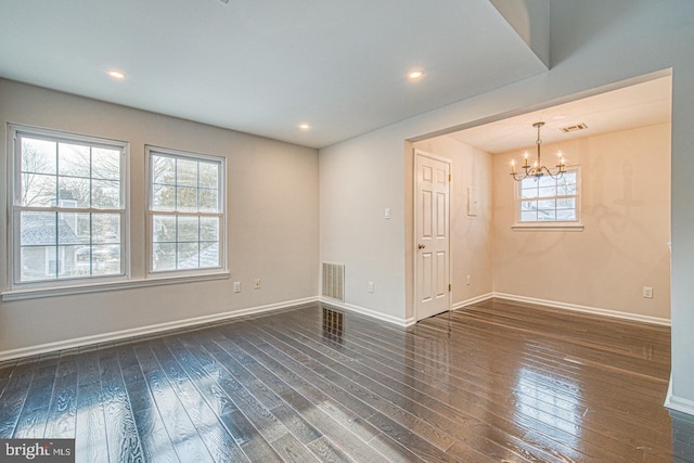 empty room with dark wood-type flooring, visible vents, and a notable chandelier