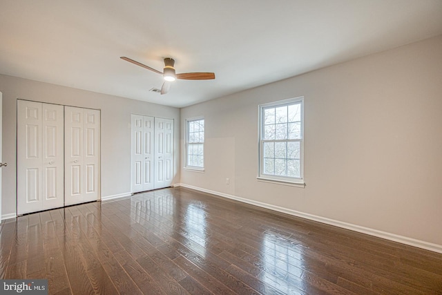 unfurnished bedroom featuring dark wood finished floors, multiple closets, visible vents, a ceiling fan, and baseboards