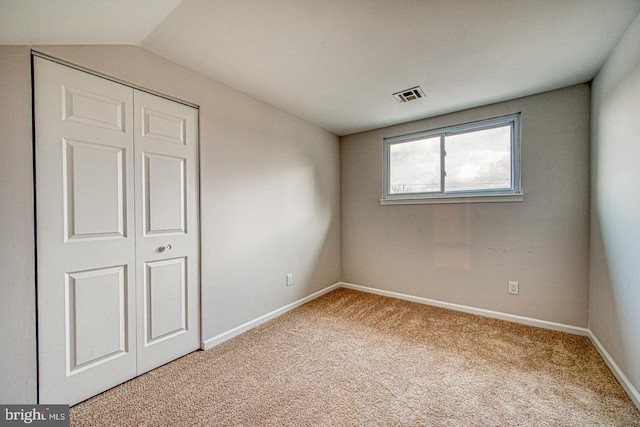 unfurnished bedroom featuring baseboards, visible vents, vaulted ceiling, carpet flooring, and a closet