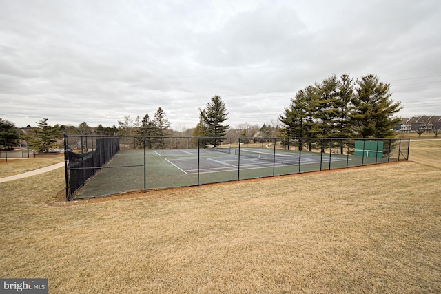 view of tennis court with a lawn and fence