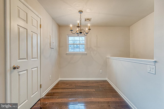 unfurnished dining area featuring dark wood-style floors, a chandelier, visible vents, and baseboards