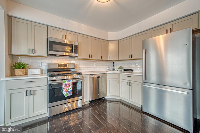 kitchen with dark wood finished floors, stainless steel appliances, light countertops, backsplash, and a sink