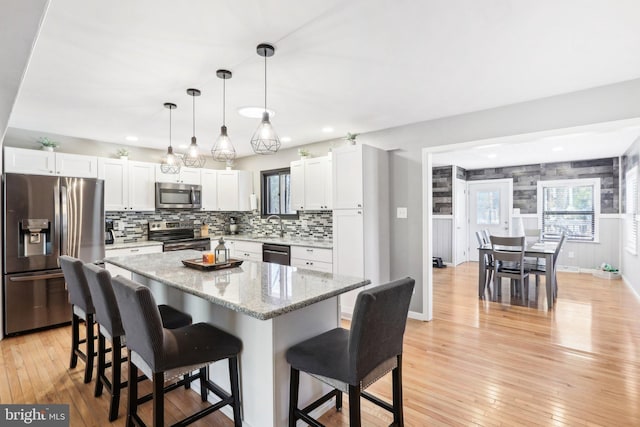 kitchen with white cabinetry, stainless steel appliances, a center island, light stone counters, and decorative light fixtures