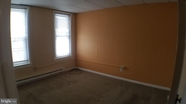 carpeted empty room with a baseboard heating unit and a paneled ceiling