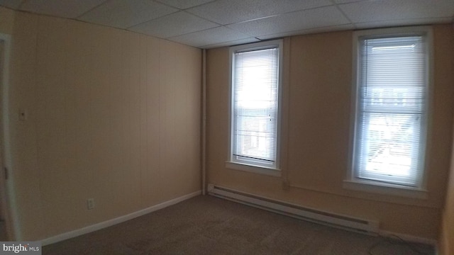 empty room featuring a paneled ceiling, a wealth of natural light, and baseboard heating