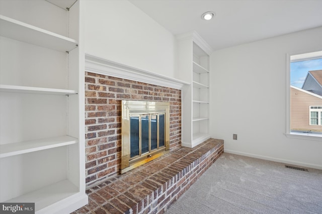 unfurnished living room with a brick fireplace, carpet flooring, and built in shelves