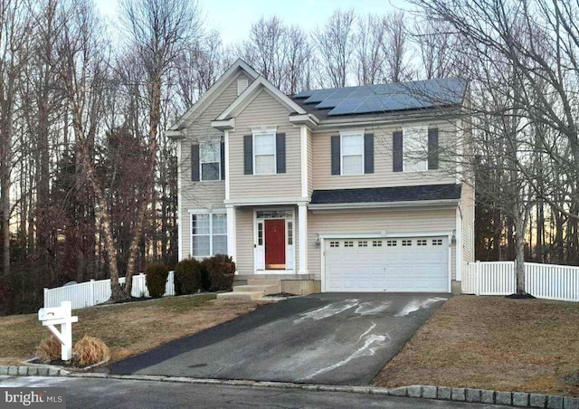 traditional-style house with a garage, roof mounted solar panels, fence, and aphalt driveway