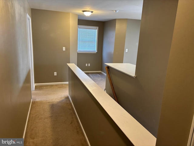 hallway with baseboards, dark carpet, and an upstairs landing