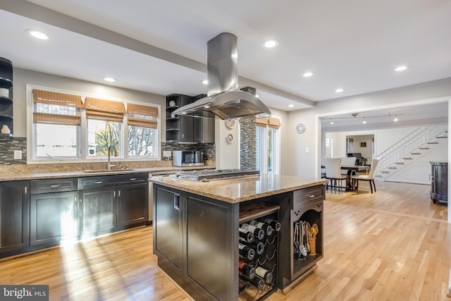 kitchen with sink, a center island, island exhaust hood, light stone countertops, and light hardwood / wood-style floors