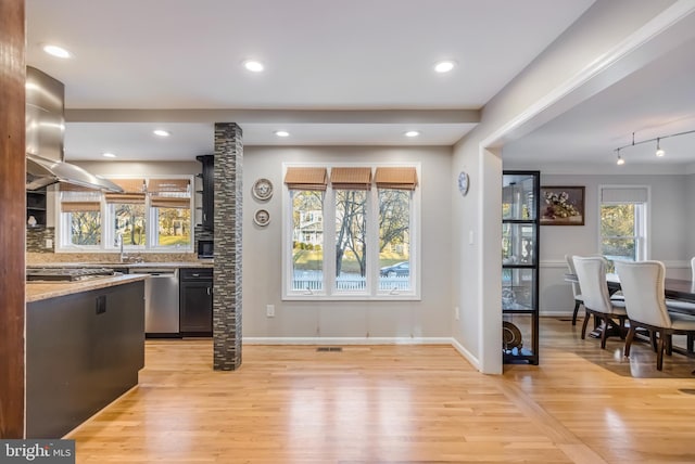 kitchen featuring light stone counters, light wood-type flooring, appliances with stainless steel finishes, island exhaust hood, and backsplash