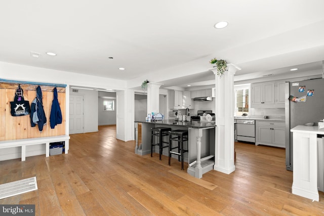 kitchen with light hardwood / wood-style flooring, a breakfast bar, dishwasher, white cabinets, and ornate columns