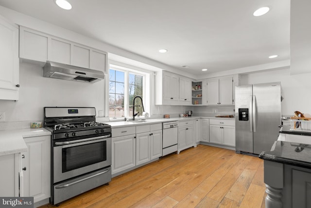 kitchen with appliances with stainless steel finishes, exhaust hood, white cabinets, and light wood-type flooring