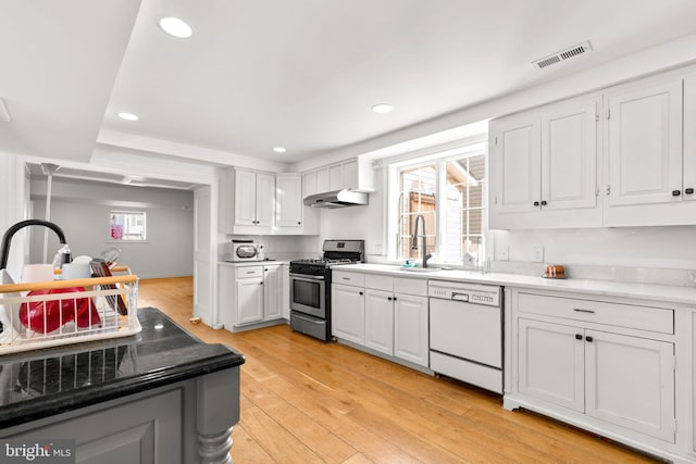 kitchen with sink, dishwasher, stainless steel gas range oven, white cabinets, and light wood-type flooring