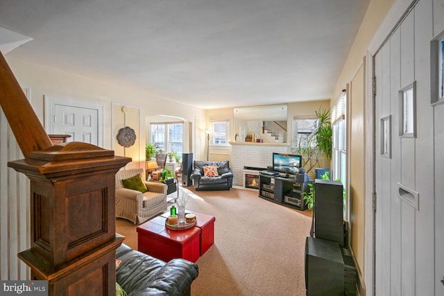 carpeted living area with arched walkways, a brick fireplace, and stairs