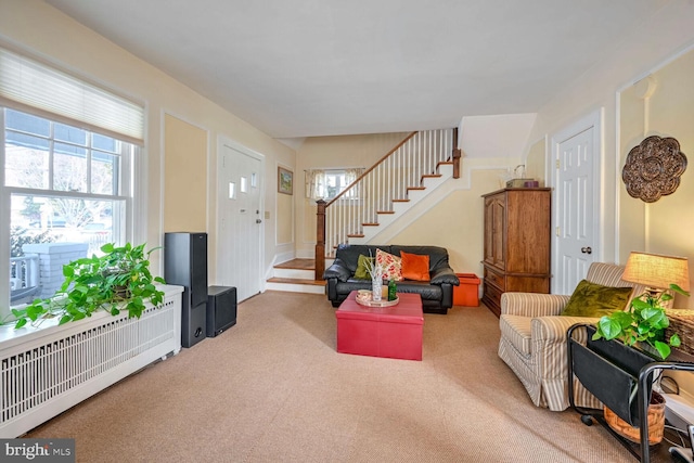 living area with a healthy amount of sunlight, carpet, radiator heating unit, and stairway