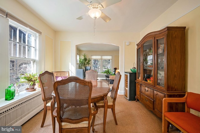 dining area with arched walkways, radiator heating unit, light carpet, and a ceiling fan